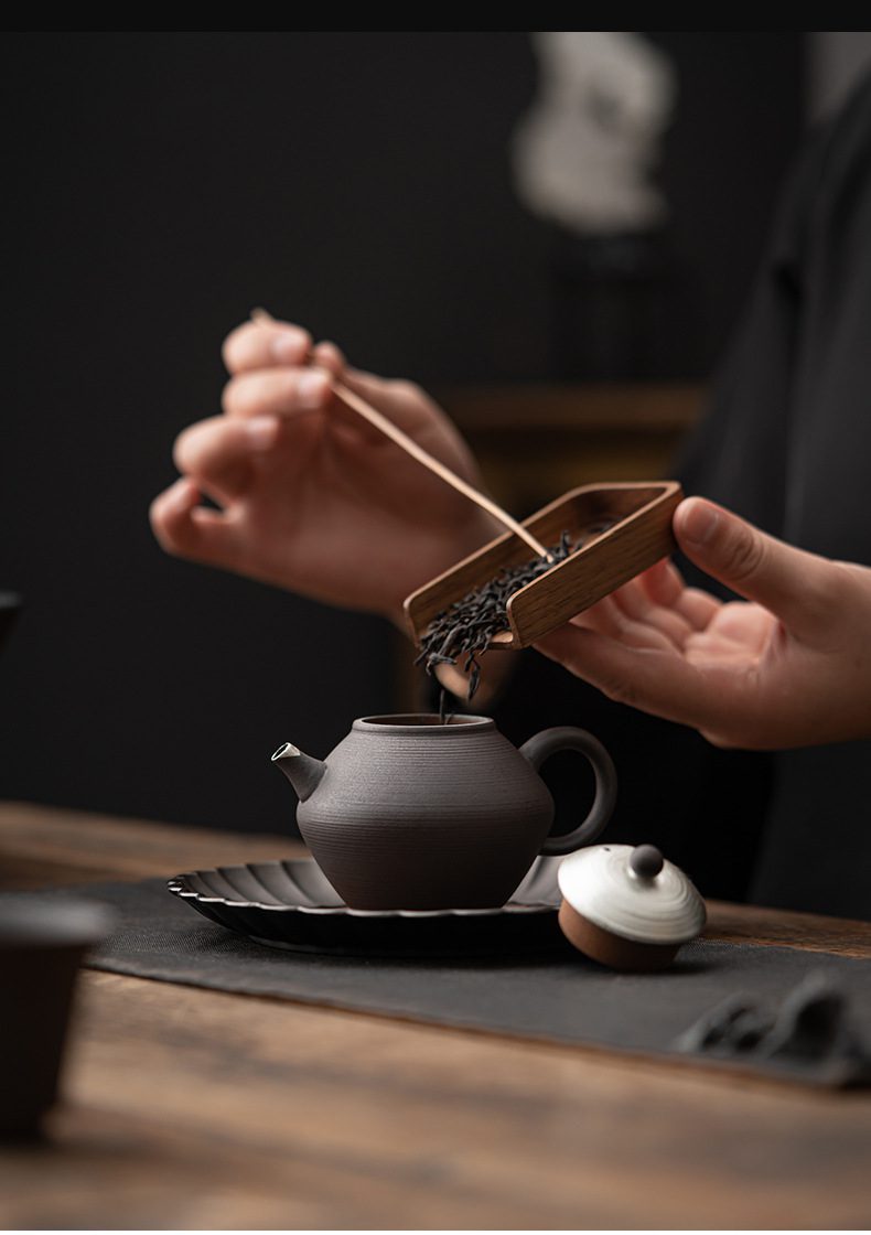 空寂老岩泥明淨茶壺，南山居手工紫砂小品壺，沉穩黑色壺身配質感木質茶則，正注入頂級烏龍茶葉，展現極致禪意茶道氛圍。