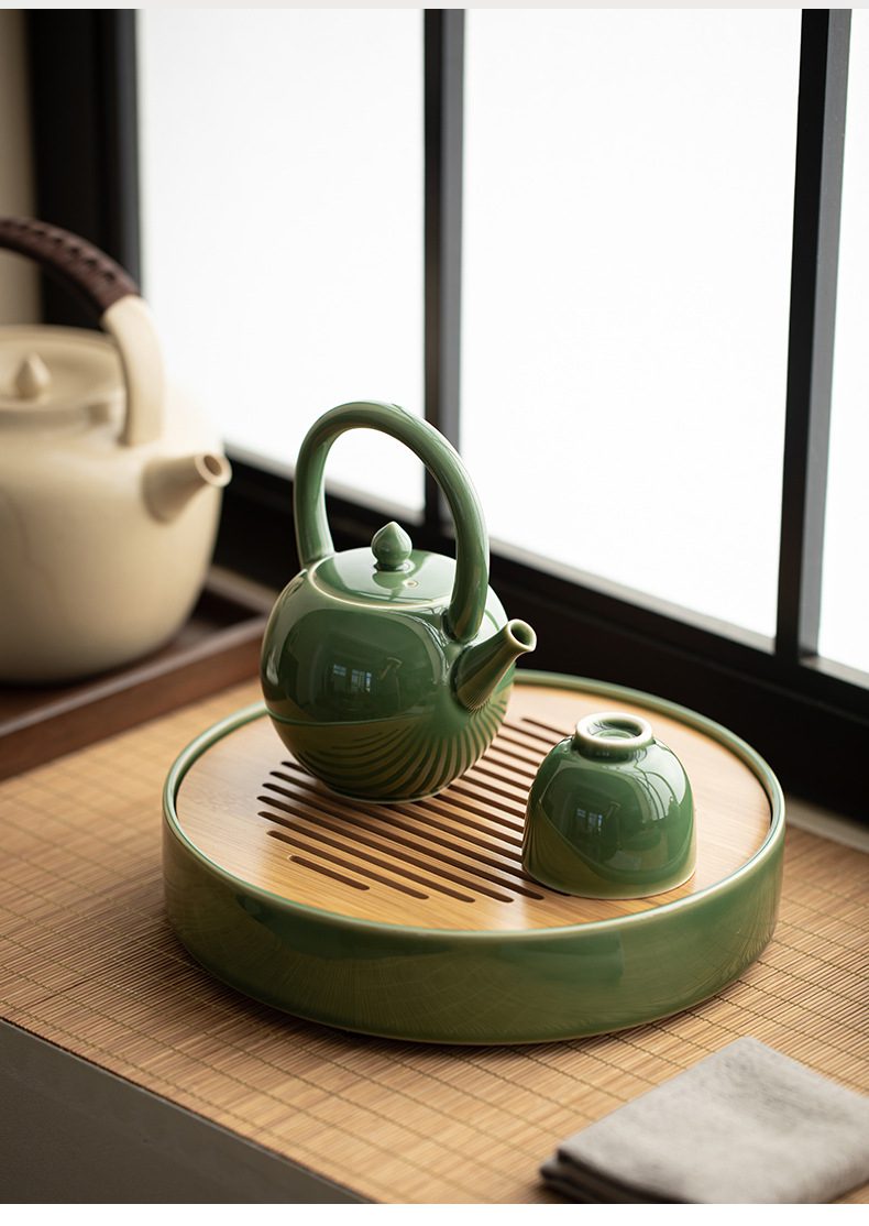 青璃釉圓月茶壺，南山居青瓷提梁壺與茶杯，釉色如玉潤澤，置於圓形竹製茶盤上，呈現簡約雅致的禪意美學。