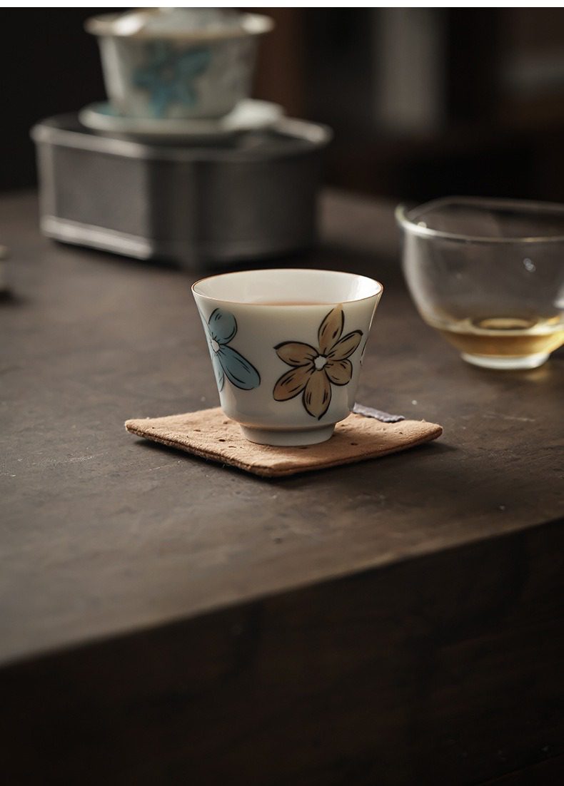 漫花品茗杯，南山居手繪花卉茶杯，釉面溫潤細膩，繪有淡雅藍黃花朵，呈現清新禪意茶席氛圍。