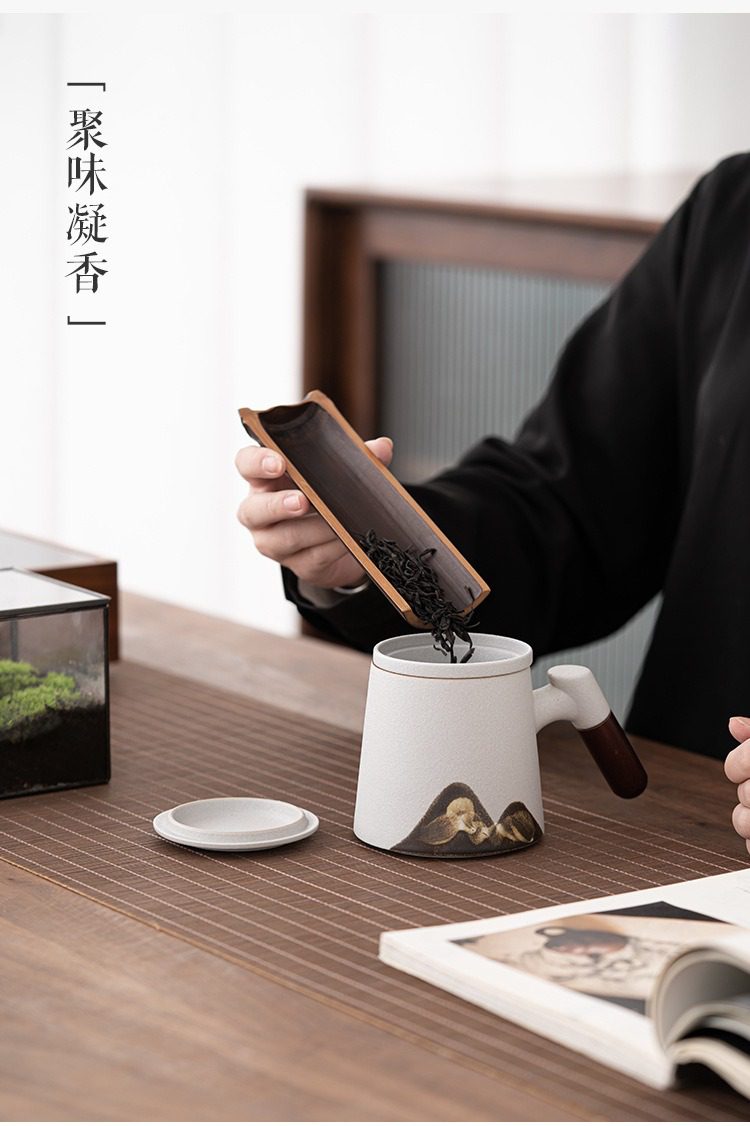 黑陶遠山雲川辦公馬克杯，南山居禪意風格手工粗陶濾茶杯，搭配天然竹製茶則，正在將乾茶葉投入杯中，呈現優雅品茗場景。