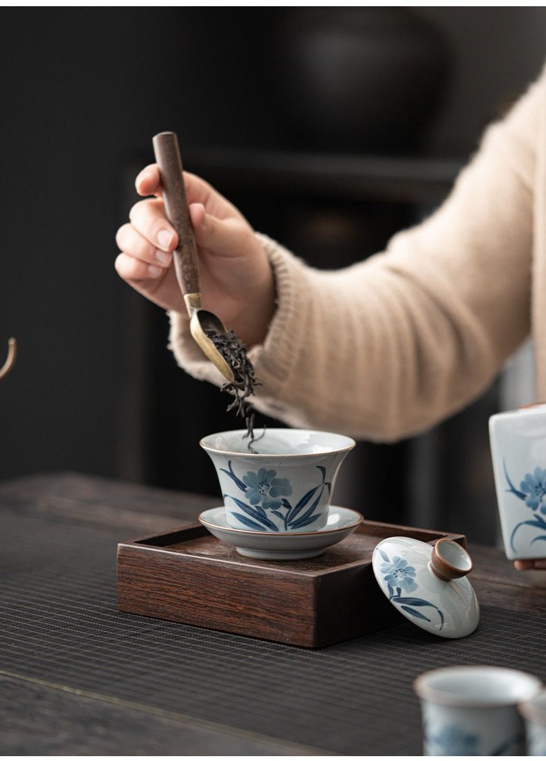 手繪功夫茶具套組，南山居青花瓷蓋碗，手繪花卉紋飾精緻典雅，搭配深色木質茶盤與銅柄茶勺，呈現傳統茶道美學。