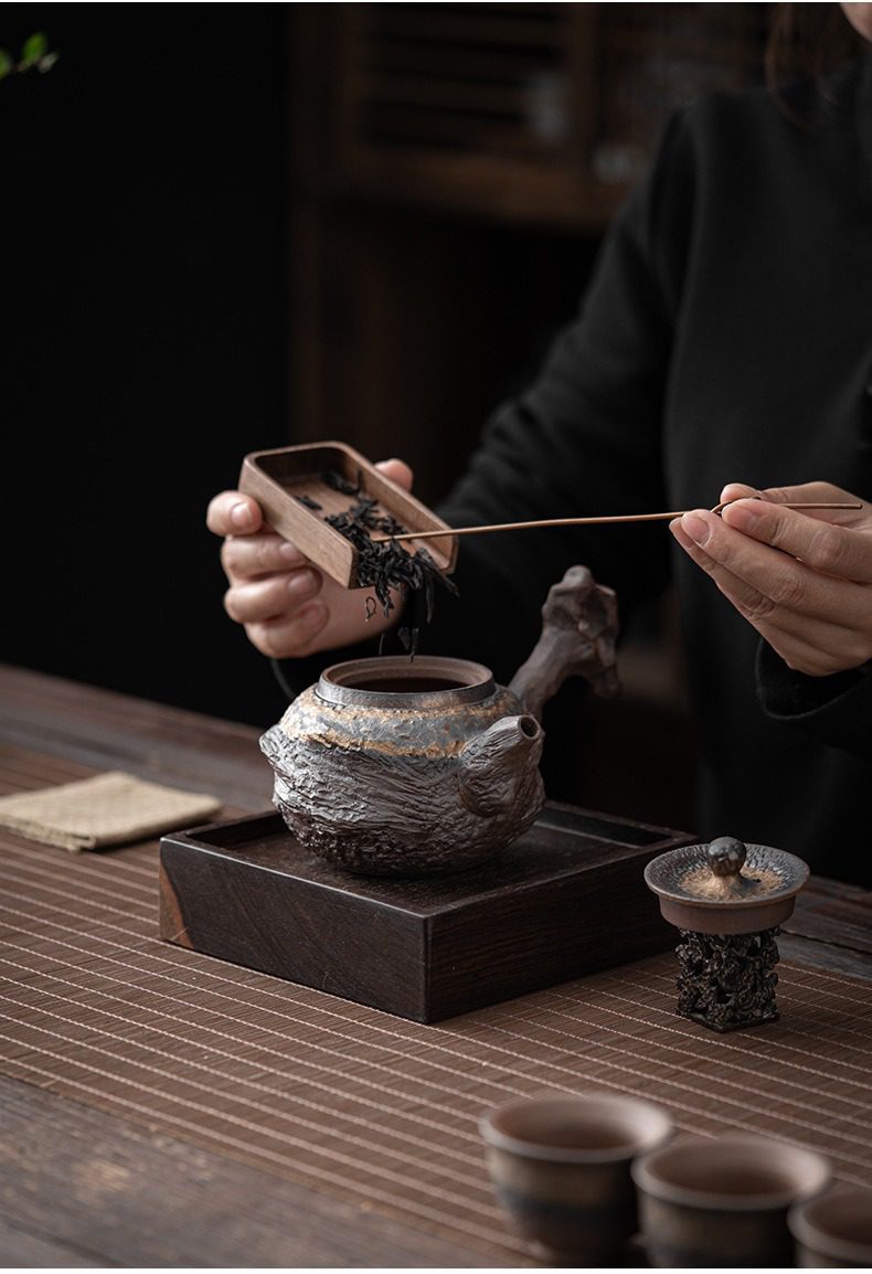 古早燒湖石側把壺，南山居手工粗陶茶壺，壺身呈現獨特岩礦肌理，搭配沉穩木質茶盤，展現古樸禪意茶道美學。