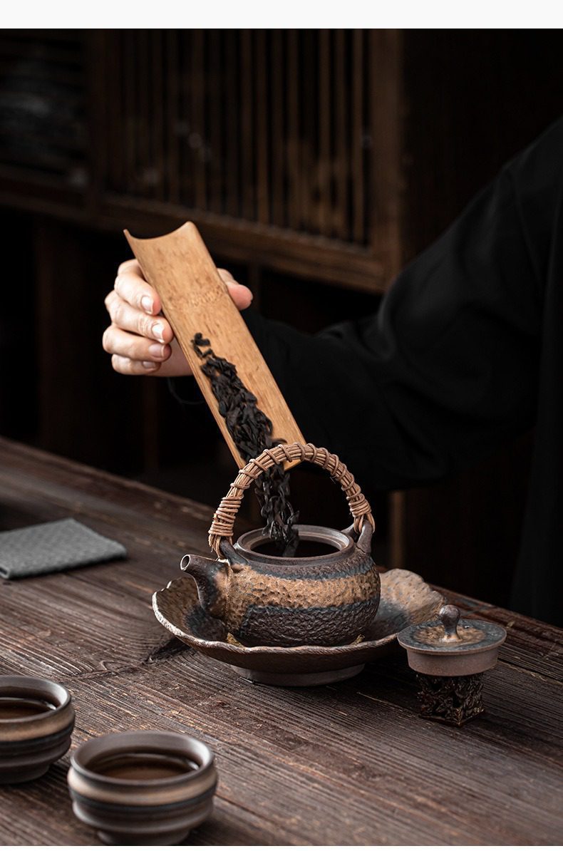 古早燒藤編提樑壺，南山居粗陶提梁壺，搭配藤編提把，正透過竹茶則緩緩將烏龍茶葉倒入壺中，展現手作茶具的樸實禪意。