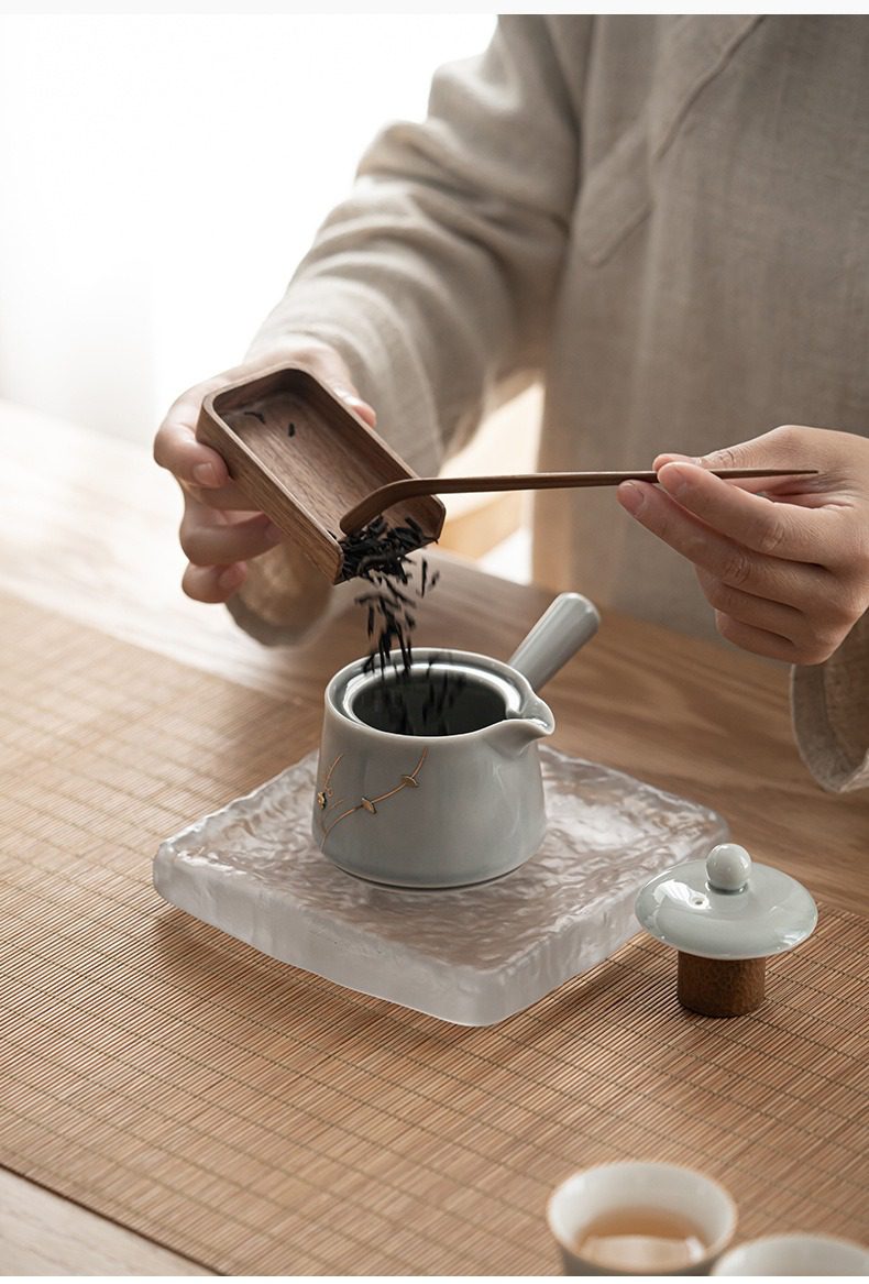 冰灰釉無由側把壺，南山居手工淺灰陶瓷茶壺，飾金色枝葉，搭配木質茶則優雅將茶葉注入，詮釋禪意茶席。