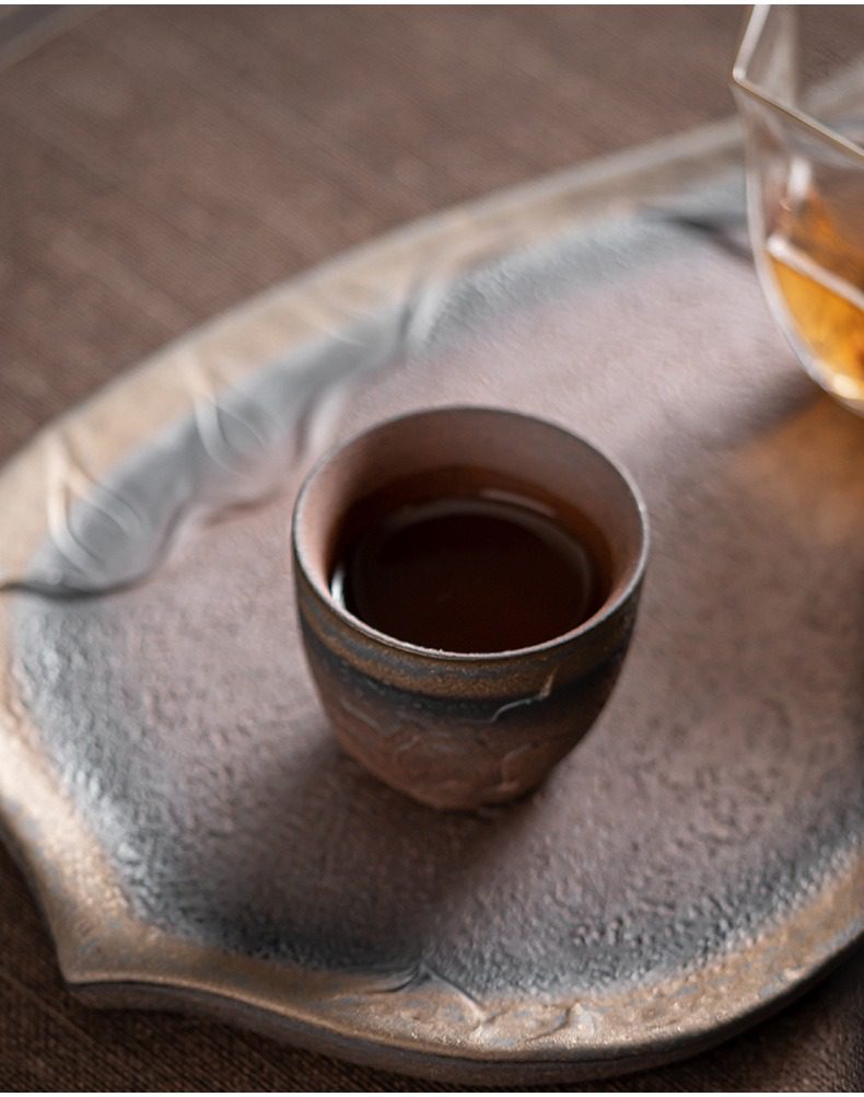 古早燒菩提品茗杯，南山居手工柴燒茶杯盛裝琥珀色茶湯，搭配質感獨特的金屬釉粗陶茶盤，呈現茶道禪意與品茗雅趣。