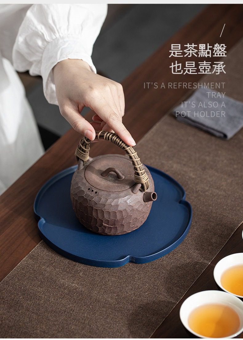 黑陶花邊乾泡茶盤，南山居粗陶手作提樑壺，壺身滿是錘目紋理，搭配藤編壺把，置於深藍花形壺承上，展現東方茶席美學。