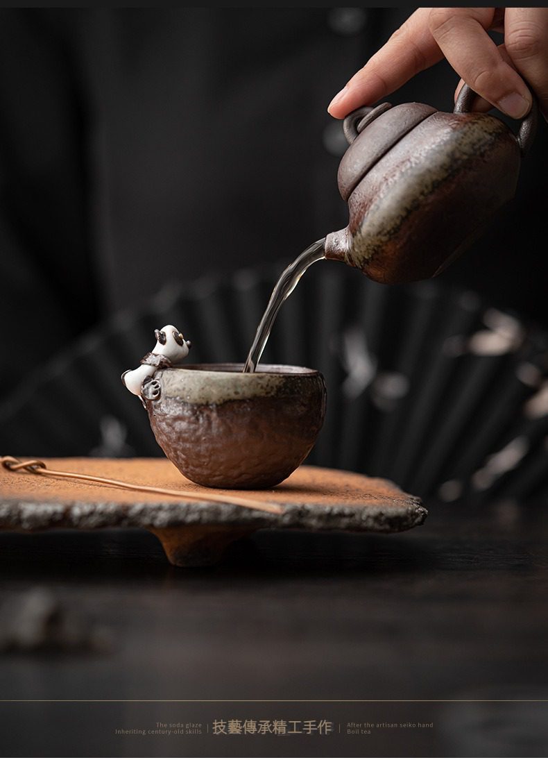 古早燒粗陶熊貓品茗杯，南山居手工粗陶茶壺正注水至可愛熊貓攀爬的茶杯，搭配質樸茶盤，展現優雅茶道美學。