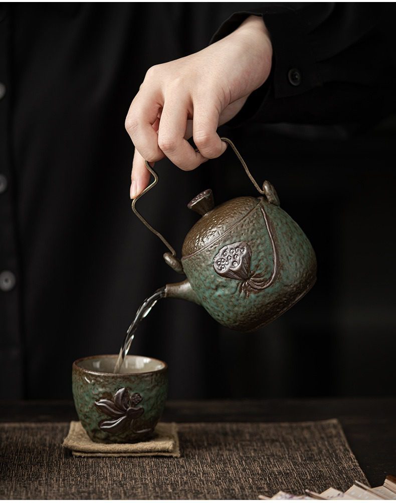 窯變青野提樑壺，南山居粗陶蓮花提樑壺與茶杯組，青綠釉面浮雕蓮蓬、荷葉，壺嘴出水流暢，茶湯傾入茶杯。