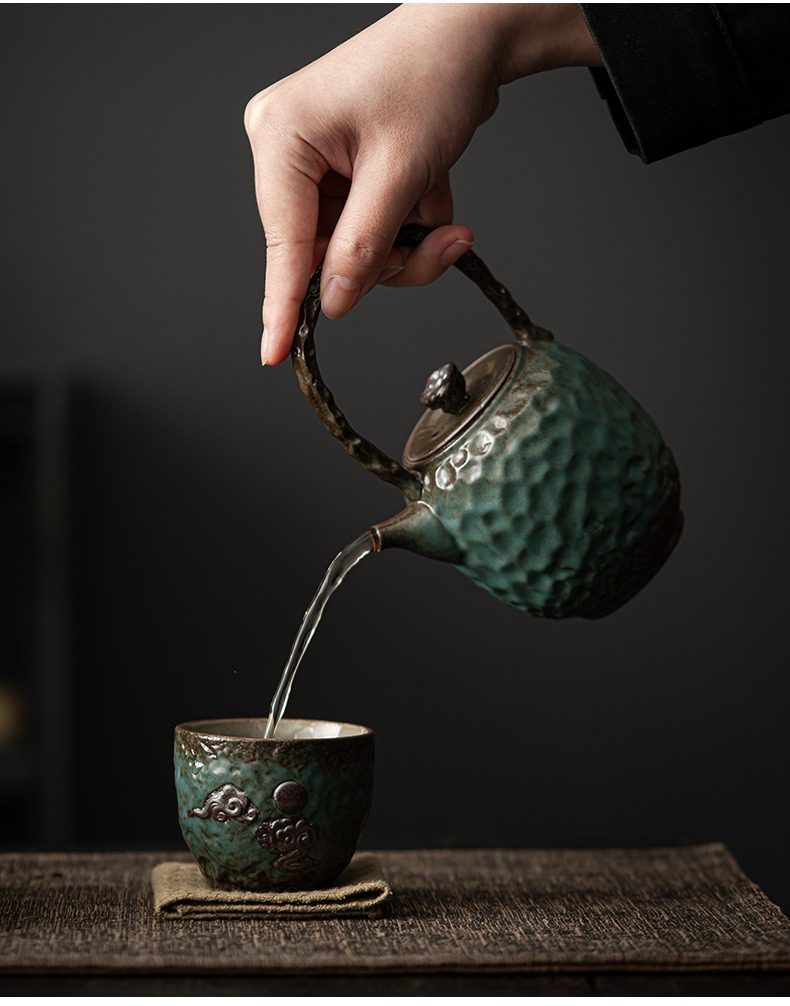 窯變青野提樑壺，南山居手作粗陶茶壺與茶杯組，深翠綠釉面呈錘紋質感，飾祥雲紋，展現品茗的雅致與禪意。