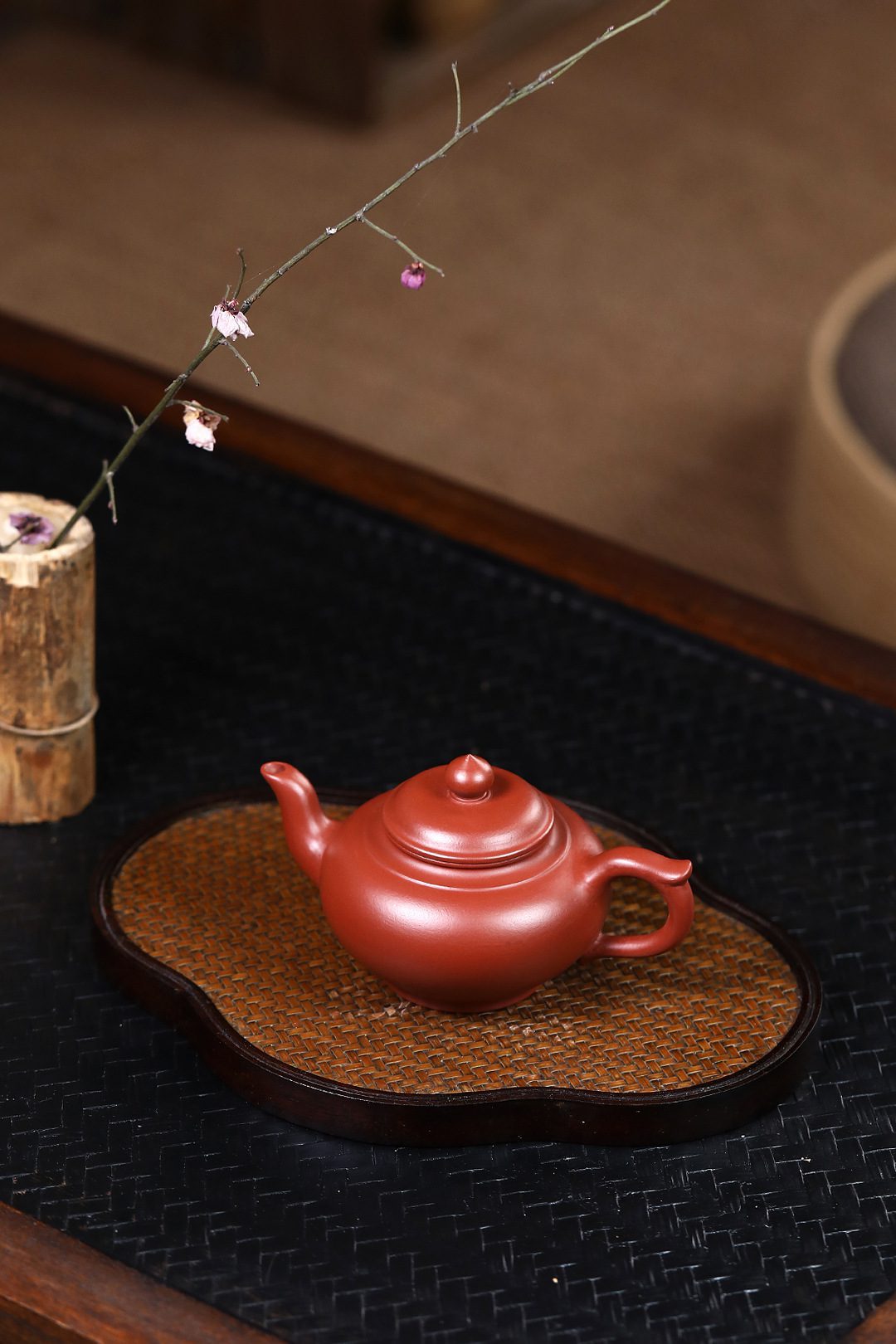 宜興紫砂壺原礦大紅袍笑櫻茶壺(130ml)，南山居手工朱泥紫砂壺，壺身呈溫潤紅棕色，置於竹編茶承上，展現精緻茶道美學。