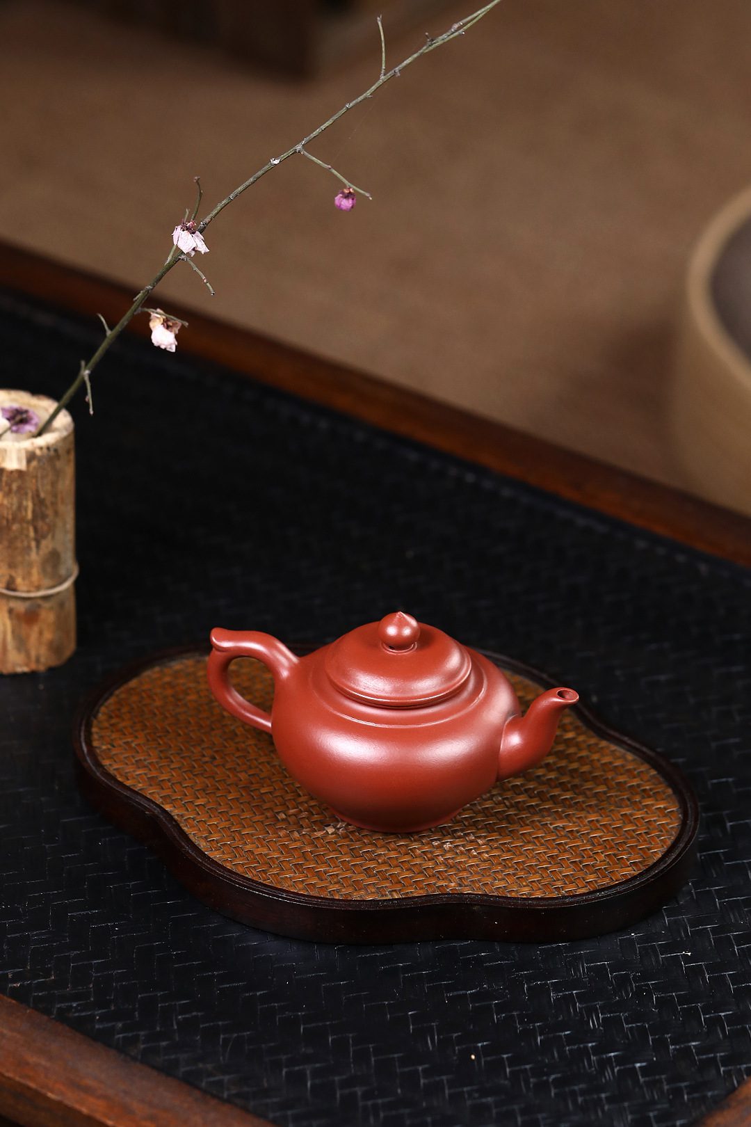 宜興紫砂壺原礦大紅袍笑櫻茶壺(130ml)，南山居手工朱泥圓壺，壺身飽滿溫潤，置於雅緻竹編茶盤上，盡顯茶席美學。
