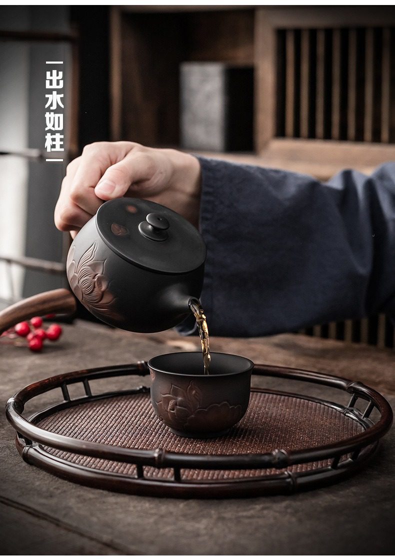 紫陶清溪荷韻茶壺，南山居黑陶蓮花浮雕蓋碗，搭配同款茶杯，出水如柱，展現精湛工藝，置於竹編茶盤。