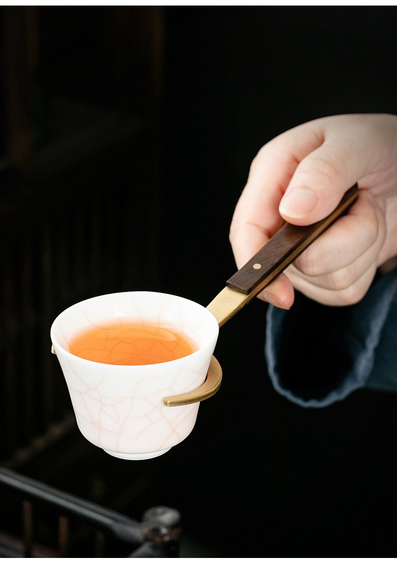 黑檀木茶道六君子杯墊套裝，南山居手工冰裂紋白瓷茶杯，盛裝琥珀色茶湯，由黃銅黑檀木茶夾輕巧持握，彰顯精緻茶具品味。