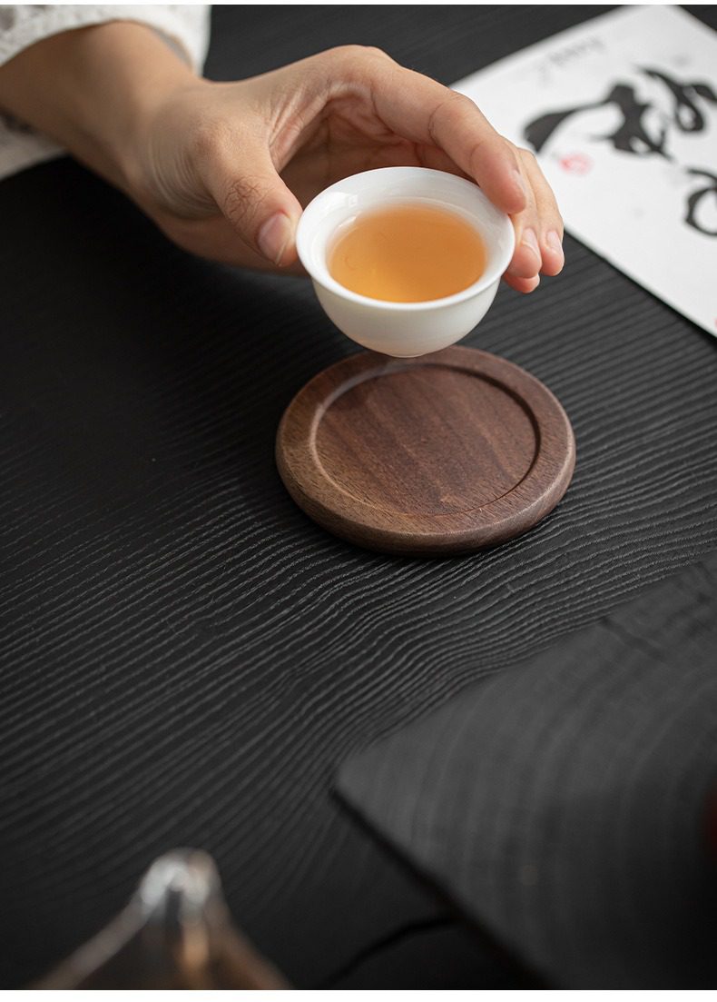 胡桃木杯墊組，南山居精緻白瓷茶杯盛裝金黃茶湯，搭配圓潤胡桃木杯墊，展現茶道優雅與手工茶具質感。