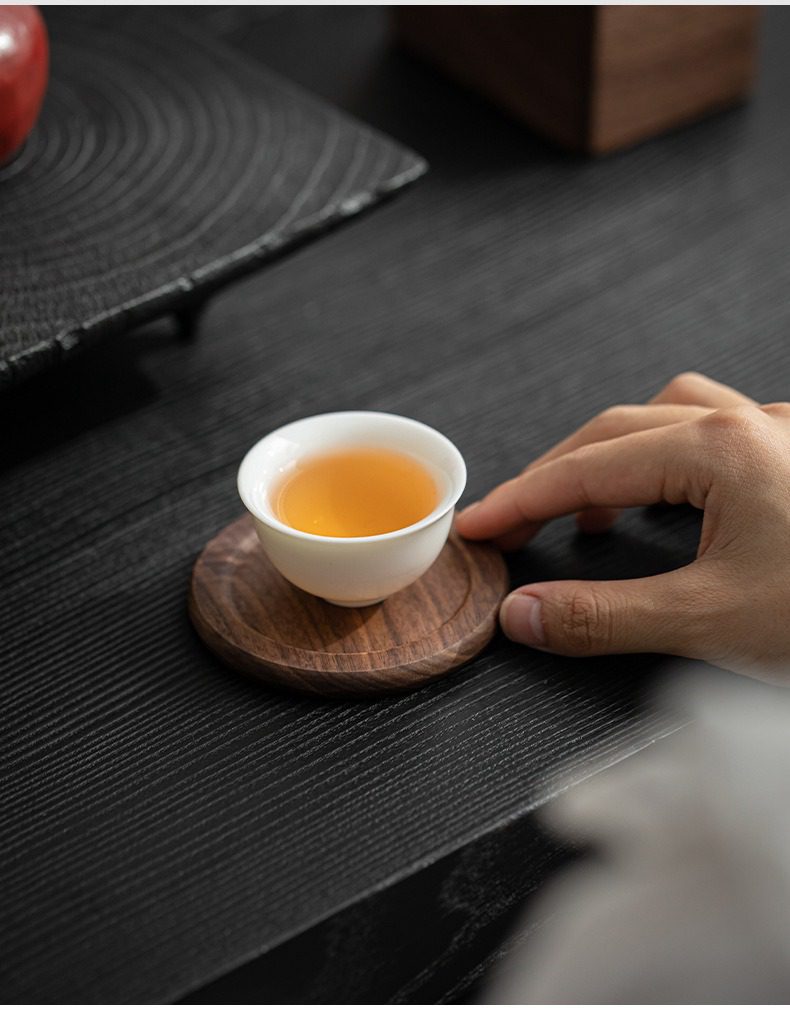 胡桃木杯墊組，南山居精緻白瓷茶杯，盛裝著琥珀茶湯，置於天然胡桃木紋杯墊上，展現茶道美學。