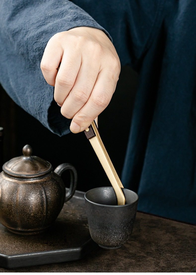 黑檀木茶道六君子杯墊套裝，南山居手工木質茶夾輕巧夾取粗陶茶杯，旁邊搭配古樸紫砂茶壺，展現茶道日常。