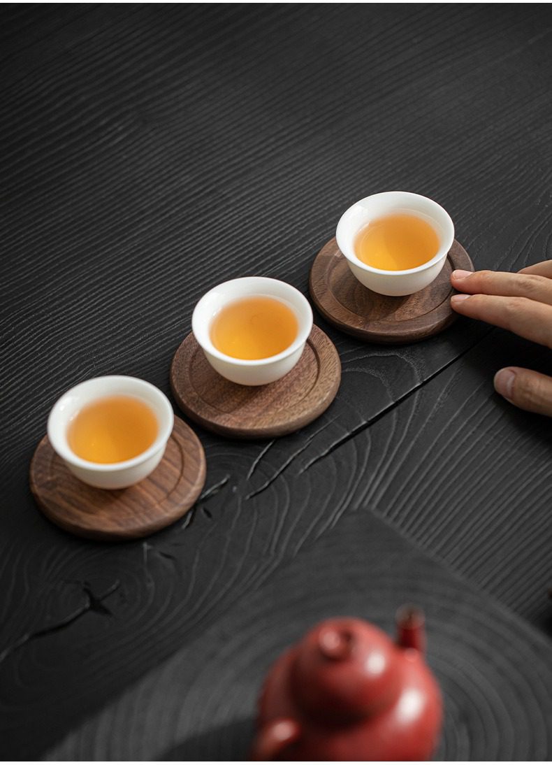 胡桃木杯墊組，南山居精緻白瓷茶杯，盛裝琥珀色茶湯，搭配溫潤木質杯墊，置於深色茶桌上，盡顯品茗雅趣。