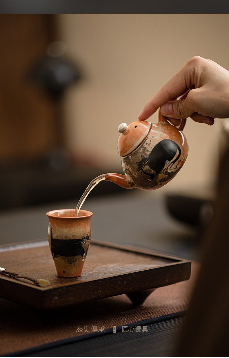 日式志野貓柴燒茶壺，南山居手工彩繪貓咪陶瓷茶壺，壺身圓潤，正將茶湯注入同款茶杯，展現精緻功夫茶具之美。