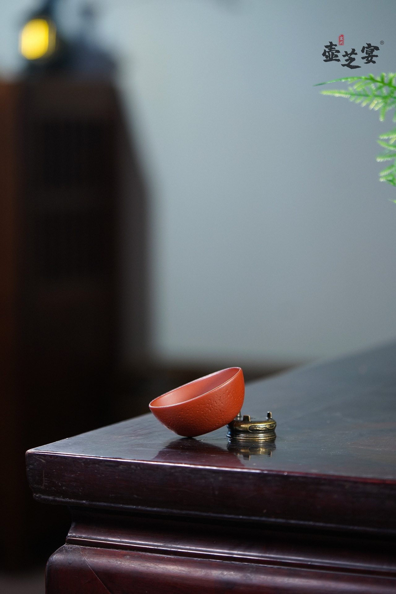 宜興原礦大紅袍元寶品茗杯，南山居手工朱泥品茗杯，泥色溫潤，杯身圓潤具獨特顆粒質感，靜置於精緻銅座上。