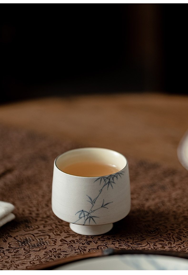 粉引白 - 手繪墨竹品茗杯，南山居手繪竹影陶瓷品茗杯，杯身米白溫潤，飾以淡雅青竹圖案，內盛金黃茶湯。