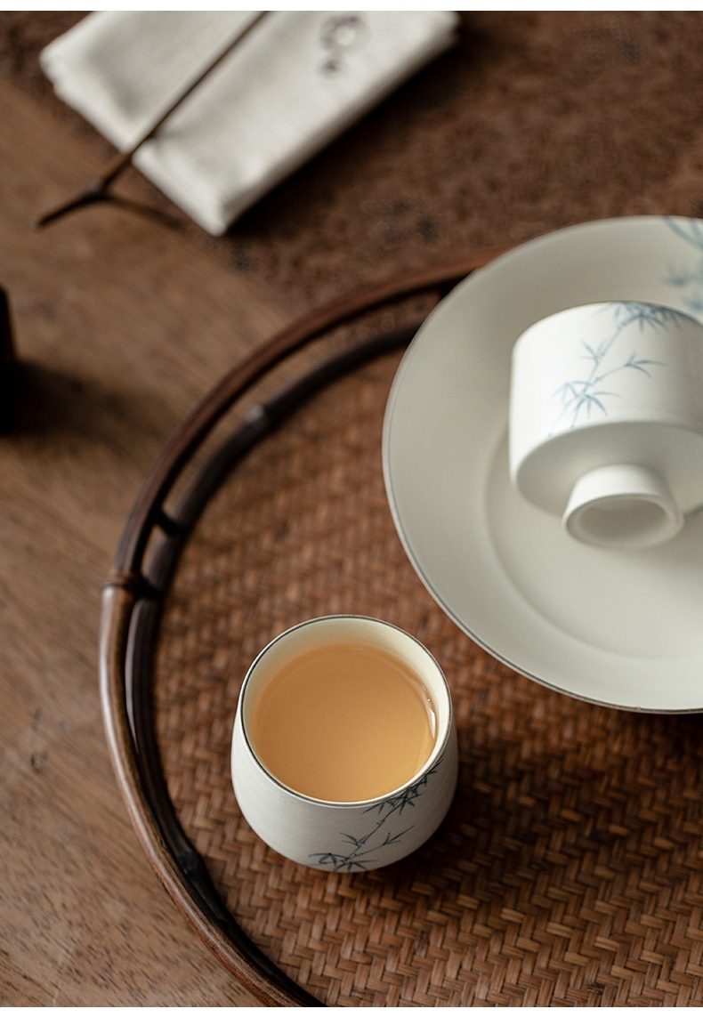 粉引白 - 手繪墨竹品茗杯，南山居白瓷手繪青竹紋品茗杯，杯中琥珀茶湯溫潤，置於竹編茶盤上，盡顯茶道雅趣。