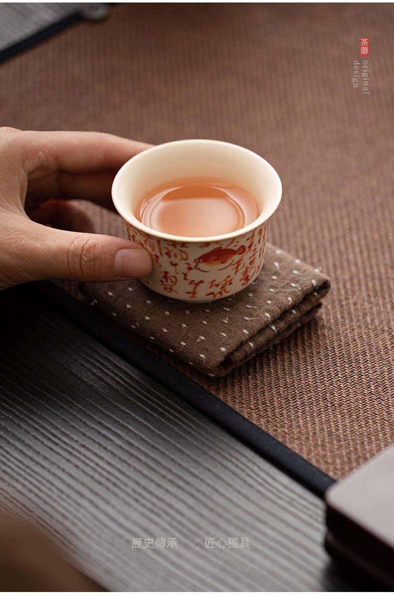 百圾碎蘇打釉品茗杯，南山居手工彩繪品茗杯，杯身飾有吉祥金魚與書法圖案，盛裝著琥珀色茶湯，展現茶席雅趣。