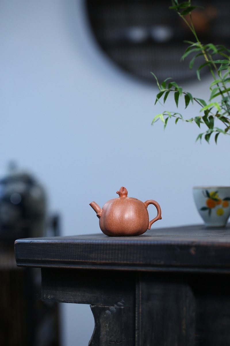 宜興紫砂壺原礦降坡泥石榴仿生壺(100ml)，南山居手工紫砂柿子壺，泥色溫潤呈赤褐，器型飽滿圓融，壺蓋鈕似柿蒂，精巧雅致。