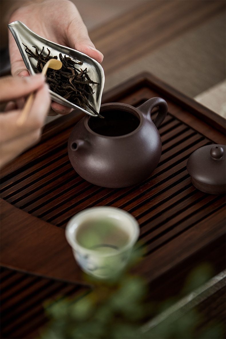 禪意手工錫蓮瓣茶則，南山居茶師以銀色茶則與竹製茶撥將烏龍茶葉置入紫砂茶壺，展現專業泡茶工藝。