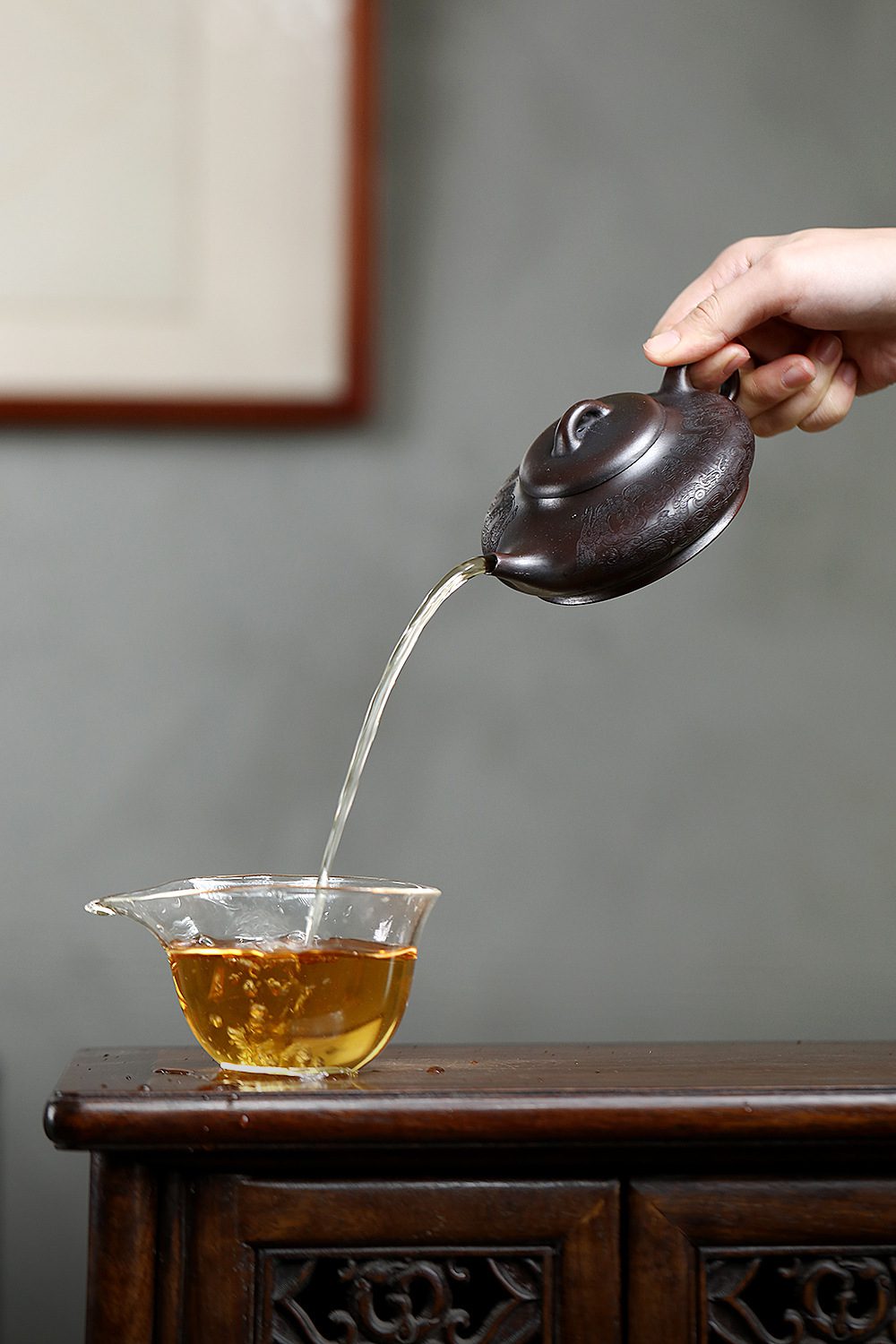 宜興紫砂壺原礦古紅泥祥瑞水扁壺(170ml)，南山居手工雕紋紫砂茶壺，深褐壺身浮雕精美紋飾，茶湯流暢注入晶瑩公道杯，展現優雅茶道。