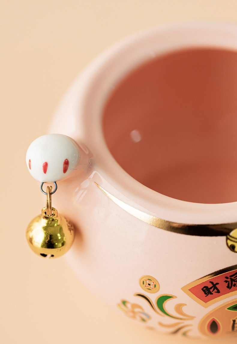 招財兔茶葉罐，南山居粉色陶瓷招財茶罐，飾有金色「財源」字樣與吉祥圖案，並懸掛精緻招財貓吊飾與金鈴，用於儲存茶葉。