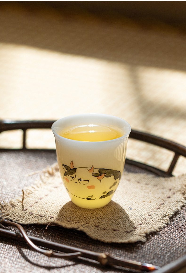 白皙玉泥十二生肖品茗杯，南山居手繪萌牛陶瓷品茗杯，杯身圓潤，圖案生動有趣，盛裝金黃茶湯。