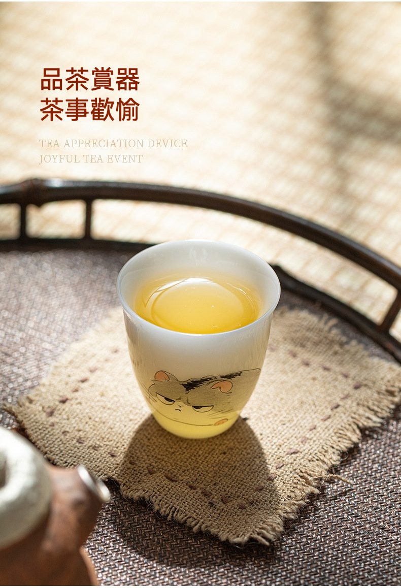 白皙玉泥十二生肖品茗杯，南山居原創手繪陶瓷品茗杯，杯身卡通貓咪圖案生動，盛滿金黃茶湯，展現茶具精緻與趣味。