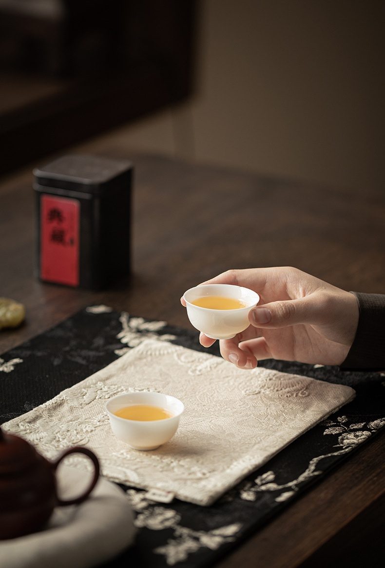 梅花刺繡織錦茶席桌巾壺承，南山居精緻白瓷品茗杯，瓷質細潤如玉，盛裝金黃茶湯，盡顯茶道雅韻。