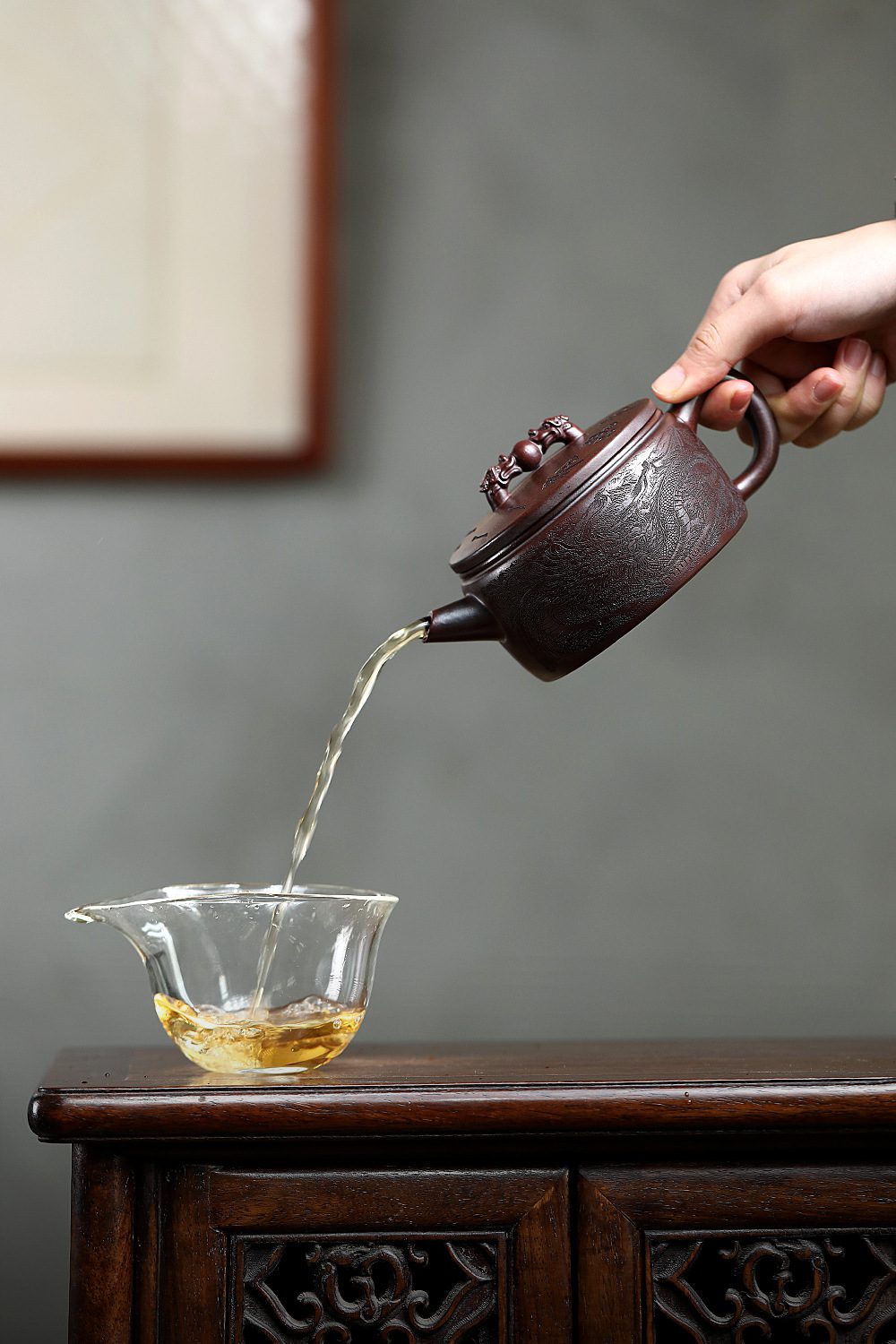 宜興紫砂壺原礦鐵血紅砂雙龍戲珠壺(250ml)，南山居精緻手工紫砂壺將甘醇茶湯緩緩注入玻璃公道杯，壺身浮雕祥雲龍紋，出水流暢，雅緻專業。