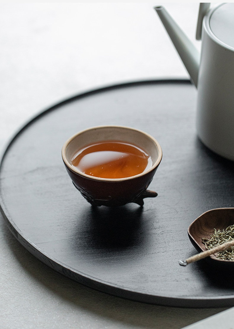 柴燒龍蛇主人杯，南山居深色手工品茗杯，盛載琥珀色茶湯，置於質感圓形茶盤上，盡顯茶道美學。