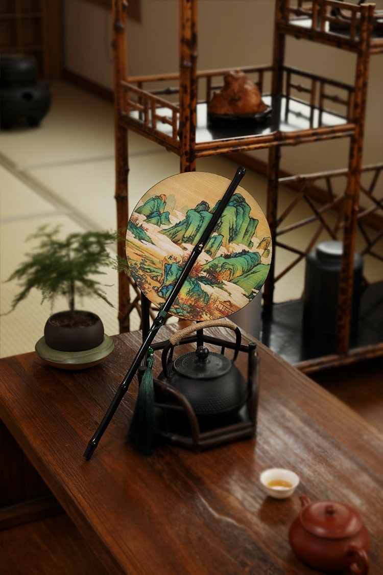 古畫竹絲腰扇，南山居茶道佈景，包括朱泥紫砂壺、日式鑄鐵壺、精緻茶杯與一把山水畫團扇，充滿禪意。