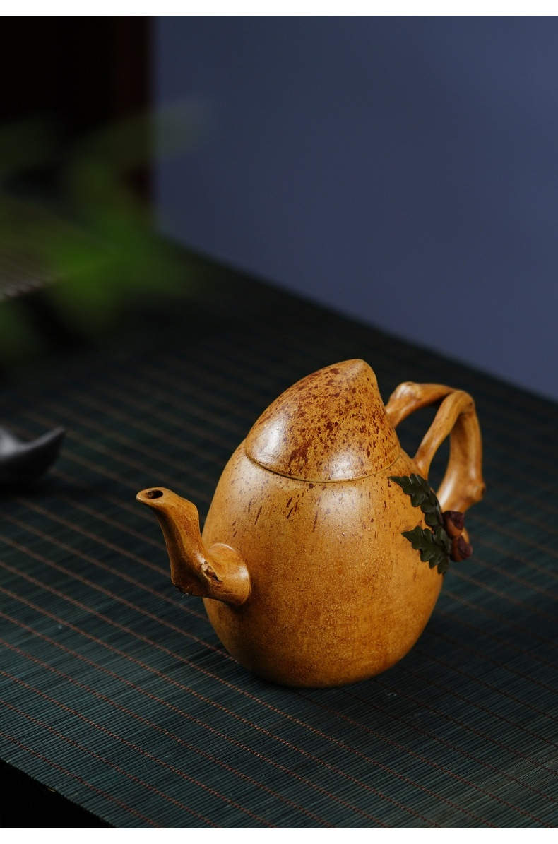 宜興紫砂壺原礦黃金段泥聖桃壺(400ml)，南山居手工仿瓜果茶壺，壺身圓潤飽滿，泥色古樸自然，壺把點綴翠綠枝葉與紅果，極具禪意。
