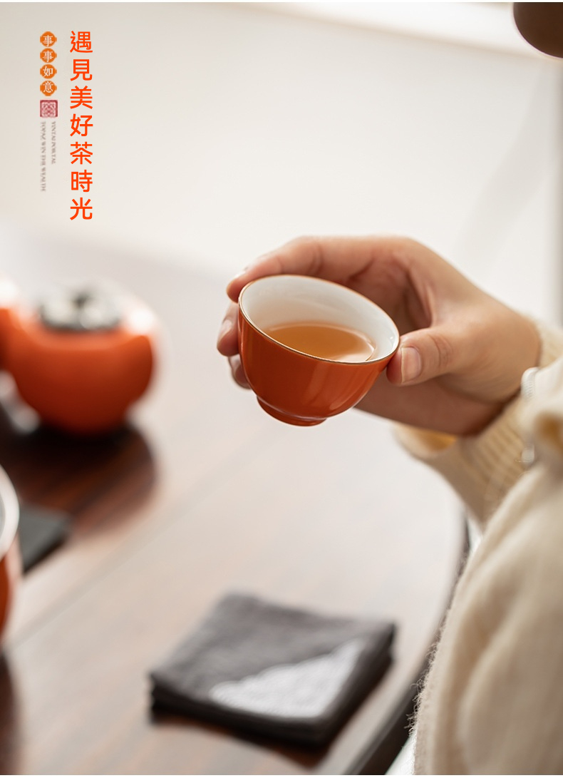 柿事如意茶具組，南山居朱紅色陶瓷品茗杯，手持一杯溫潤金黃茶湯，盡顯茶道雅趣。