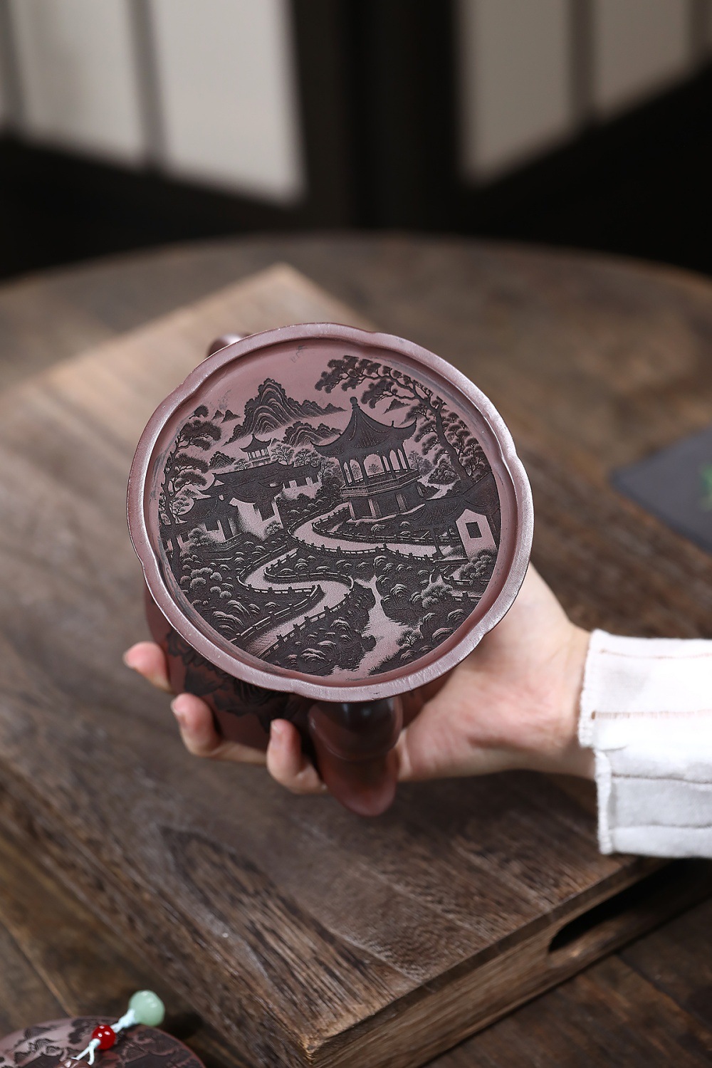 宜興紫砂壺原礦石紅泥春亭苑景壺(680ml)，南山居宜興紫砂壺蓋，蓋面精緻雕刻山水園林圖，紋理細膩，展現古典雅致的茶道美學。