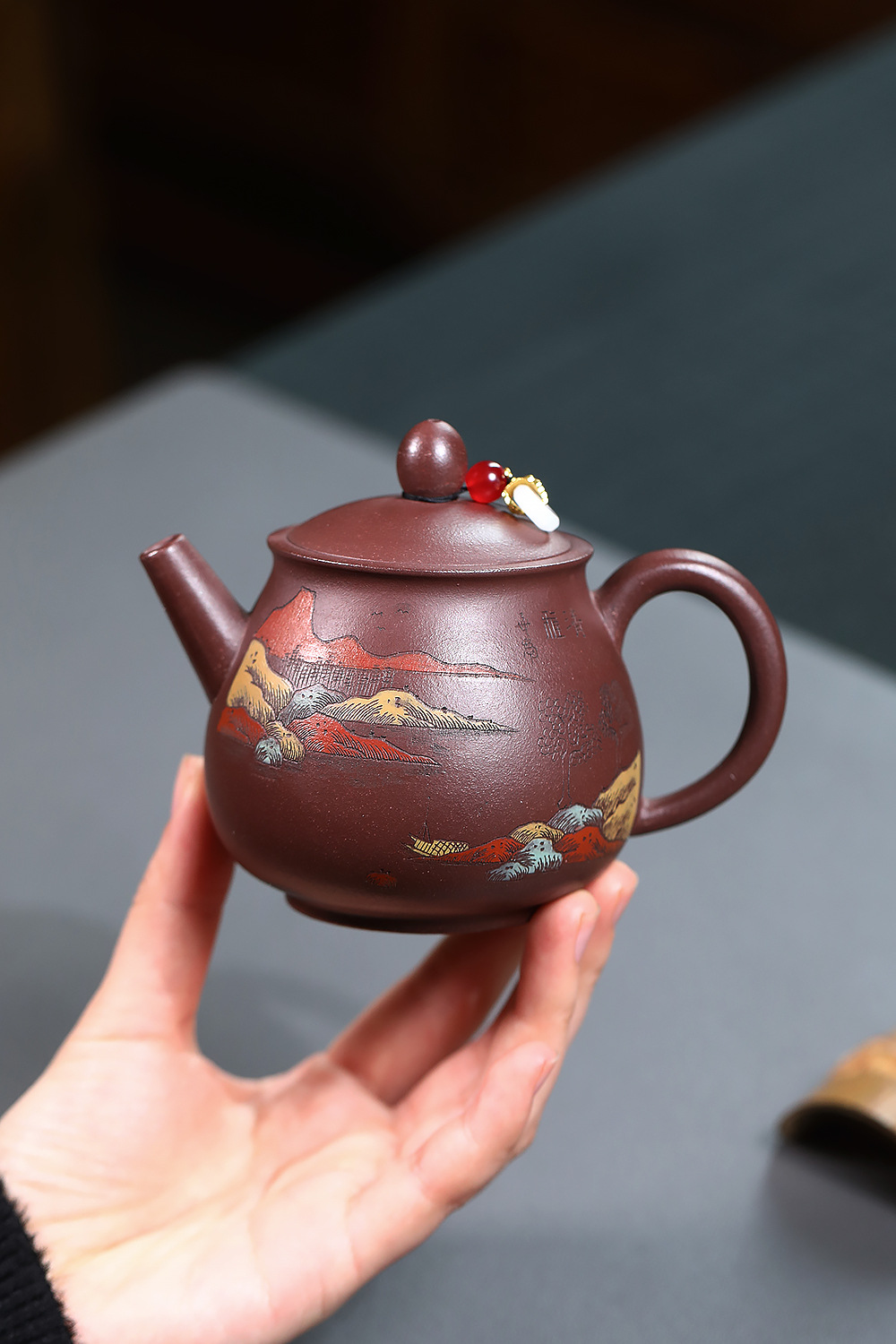 宜興紫砂壺原礦紫泥山水高潘壺(220ml)，南山居手工紫砂壺，壺身圓潤飽滿，表面繪有精緻彩繪山水圖案，壺鈕飾件獨特雅緻，為品茗增添藝術氣息。